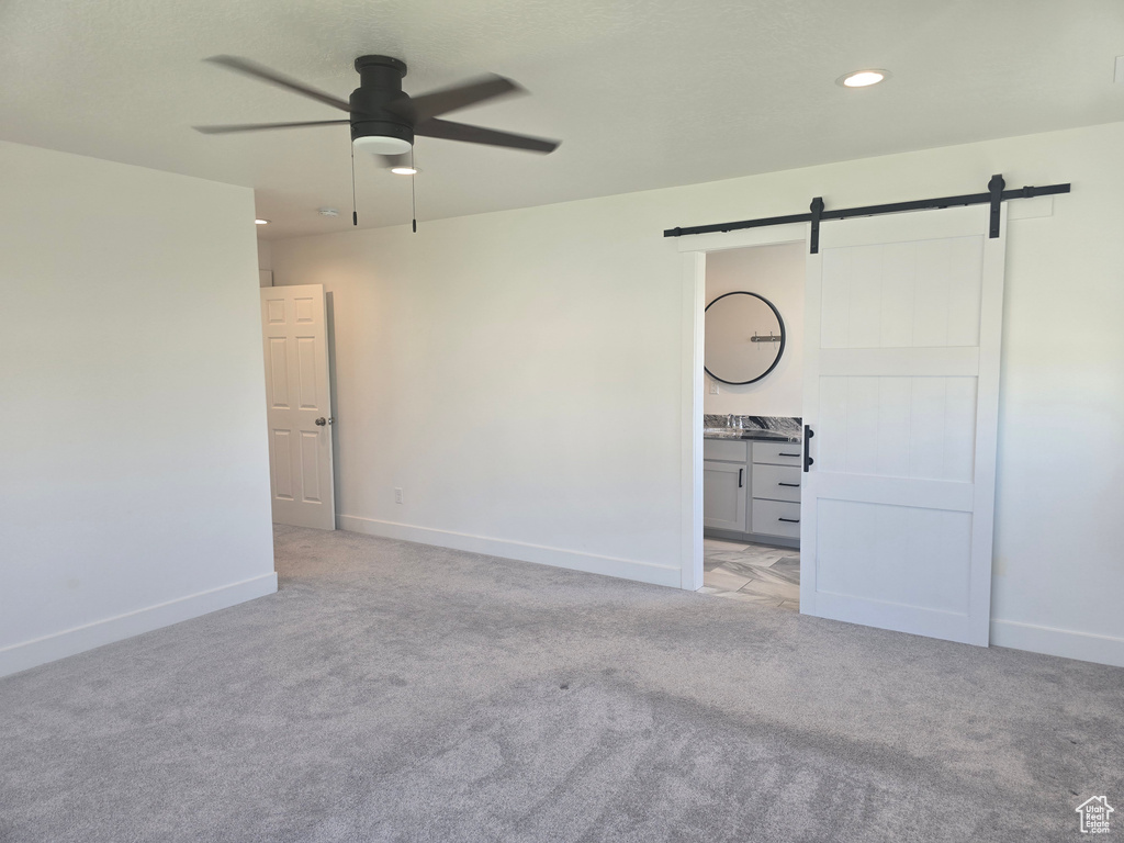 Unfurnished bedroom featuring a barn door, light carpet, baseboards, ensuite bath, and recessed lighting
