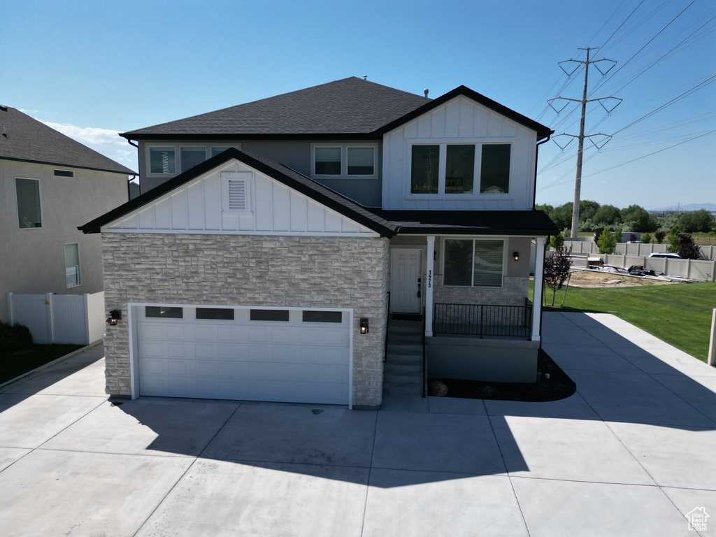 View of front facade featuring stone siding, board and batten siding, driveway, and a garage