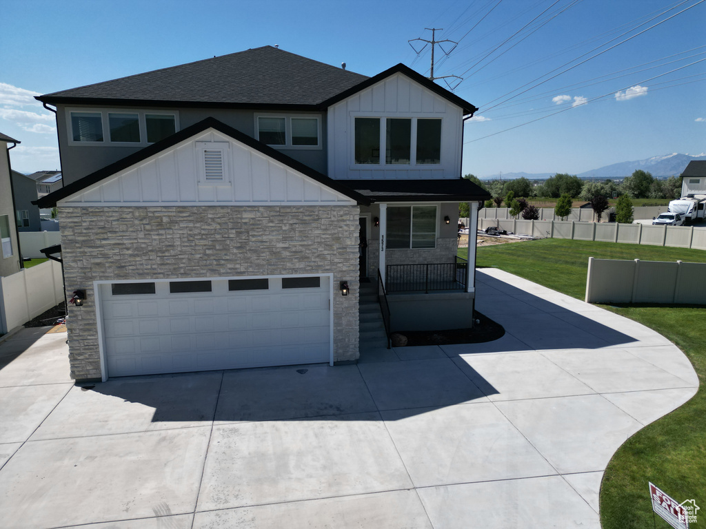 View of front of house featuring stone siding, roof with shingles, board and batten siding, driveway, and a porch