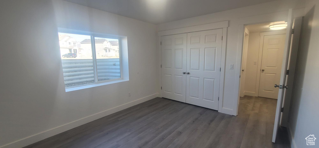 Unfurnished bedroom featuring baseboards, dark wood-type flooring, and a closet