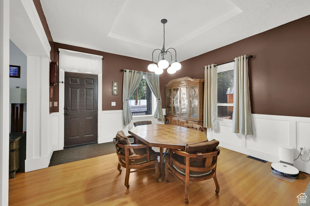 Dining room featuring a wainscoted wall, a decorative wall, wood finished floors, a tray ceiling, and a chandelier