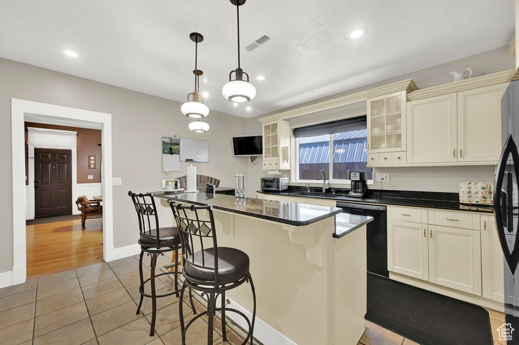 Kitchen featuring dishwasher, a sink, tile patterned flooring, a kitchen breakfast bar, and glass insert cabinets