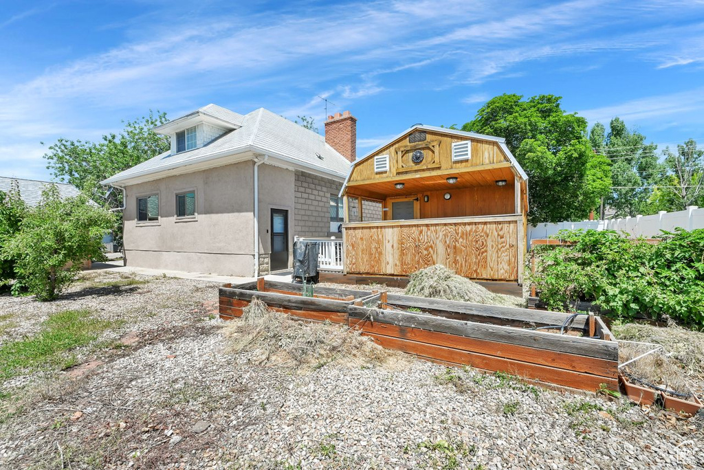 Rear view of property featuring a vegetable garden, a chimney, and stucco siding