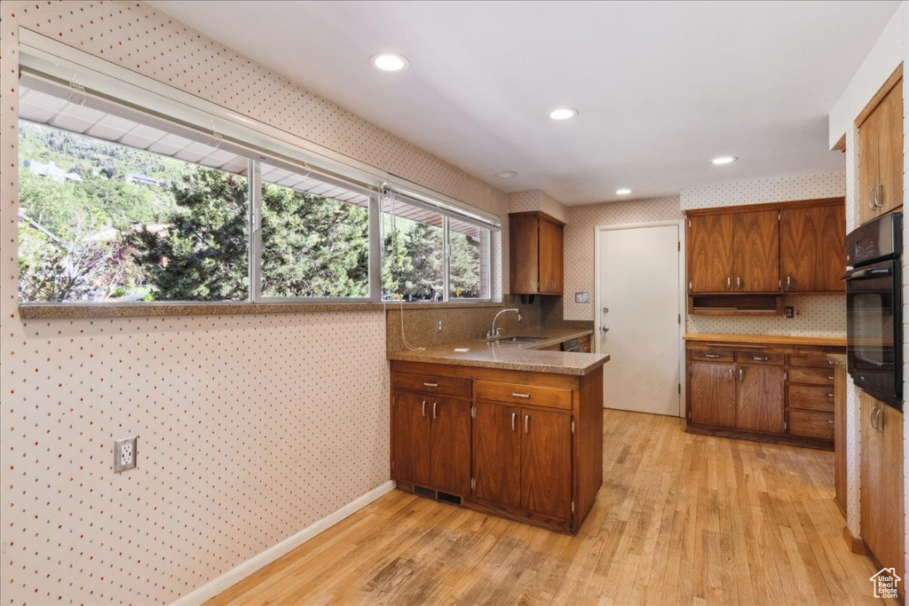 Kitchen with a sink, oven, light wood-type flooring, brown cabinets, and wallpapered walls