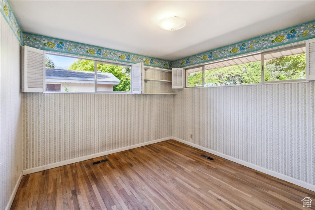 Spare room with wallpapered walls, plenty of natural light, wood finished floors, and baseboards