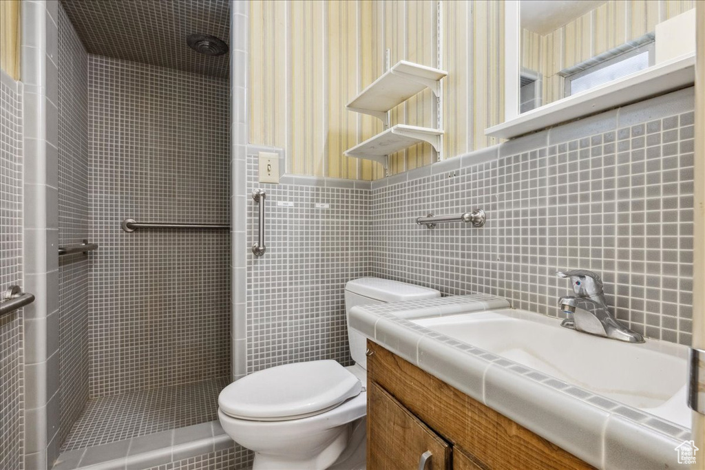 Bathroom with toilet, a tile shower, tile walls, and vanity