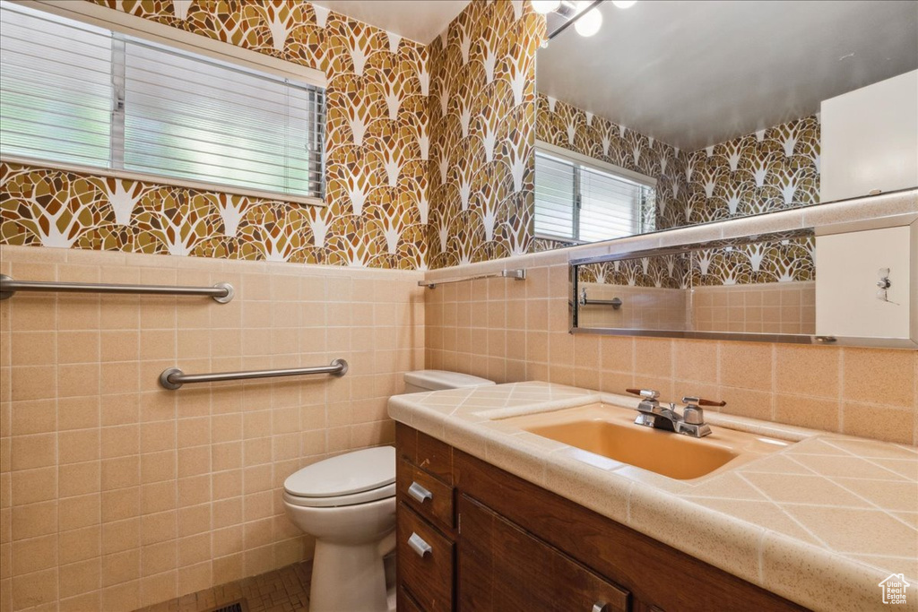 Bathroom featuring vanity, wallpapered walls, tile walls, and toilet