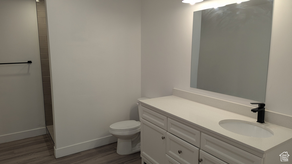 Full bath with toilet, wood finished floors, vanity, and baseboards