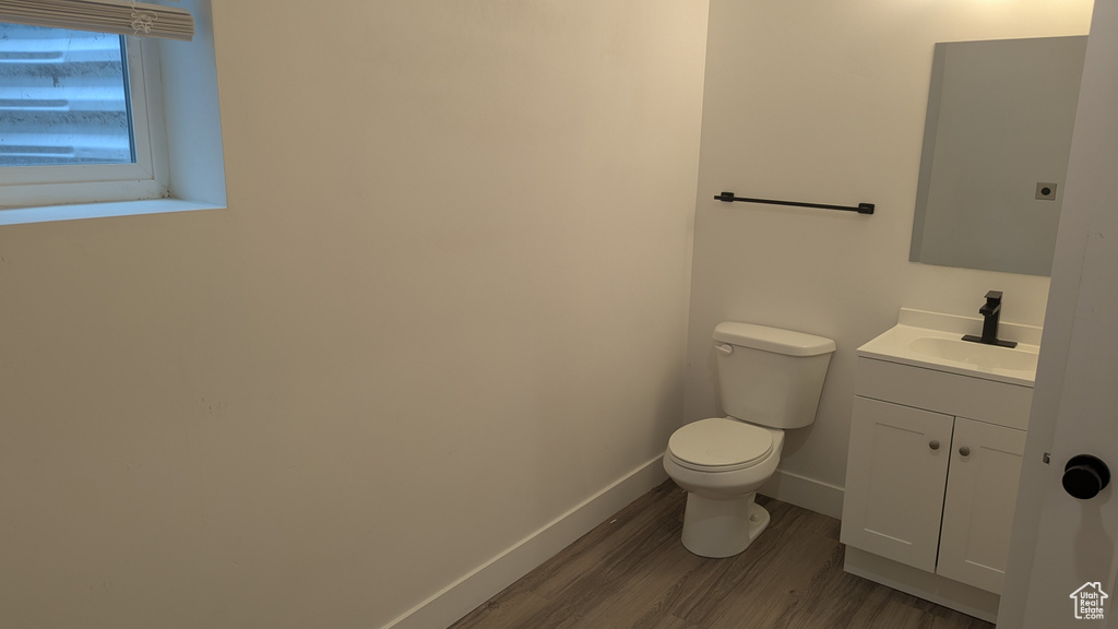 Half bath featuring wood finished floors, toilet, vanity, and baseboards