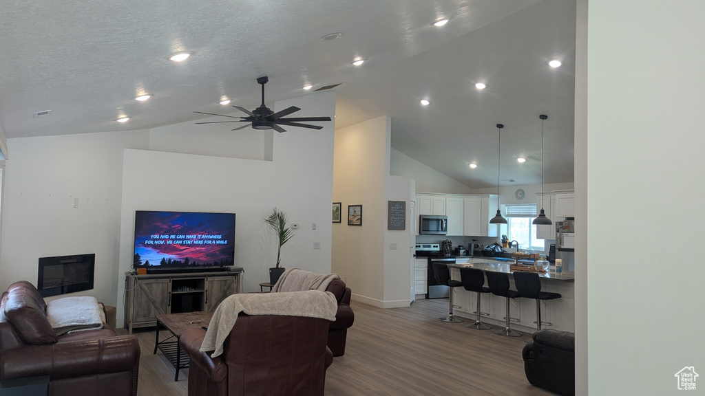 Living area featuring wood finished floors, high vaulted ceiling, a ceiling fan, and baseboards