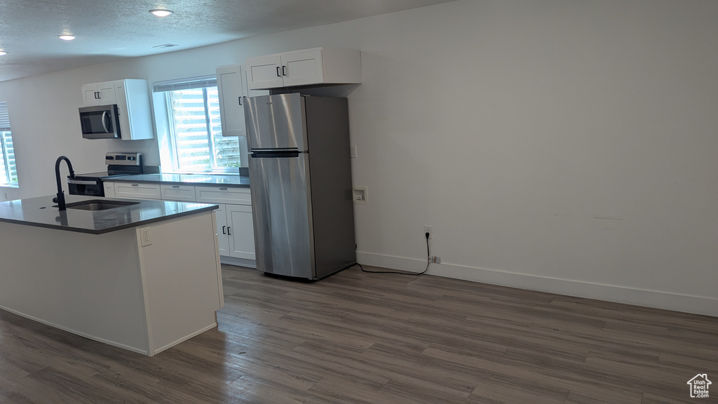 Kitchen featuring stainless steel appliances, a sink, dark wood-type flooring, white cabinetry, and baseboards