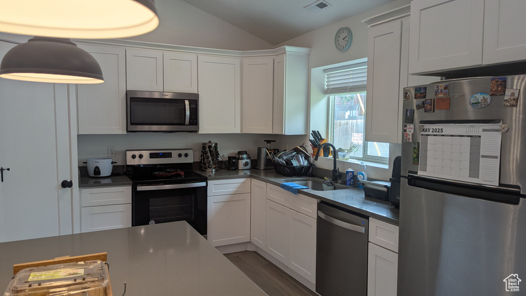 Kitchen featuring appliances with stainless steel finishes, a sink, vaulted ceiling, white cabinetry, and wood finished floors