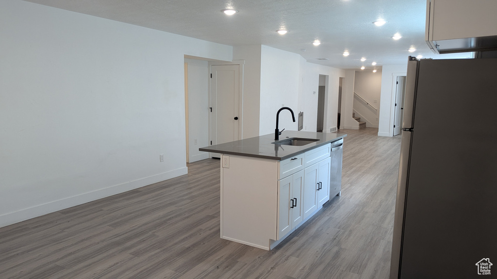 Kitchen with freestanding refrigerator, a sink, dark countertops, stainless steel dishwasher, and light wood-type flooring