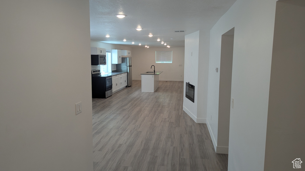 Kitchen featuring stainless steel appliances, white cabinets, a sink, light wood finished floors, and baseboards