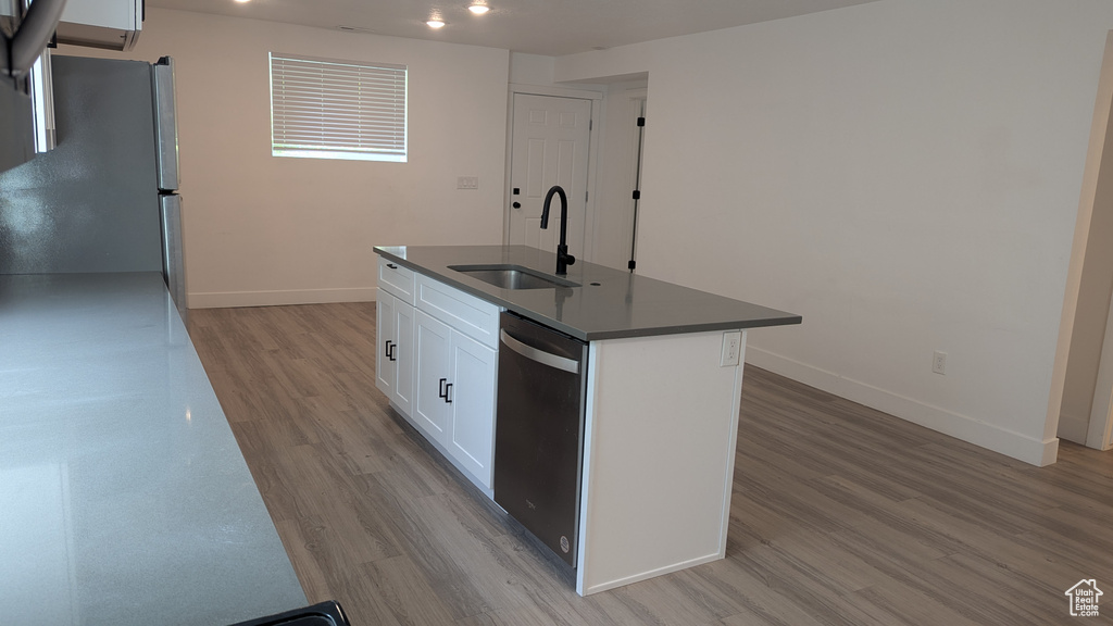 Kitchen featuring stainless steel appliances, a sink, a center island with sink, light wood finished floors, and dark countertops