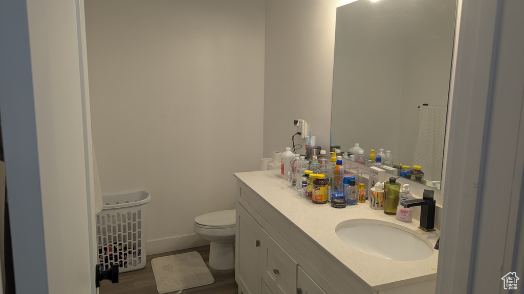 Bathroom with toilet, vanity, wood finished floors, and baseboards