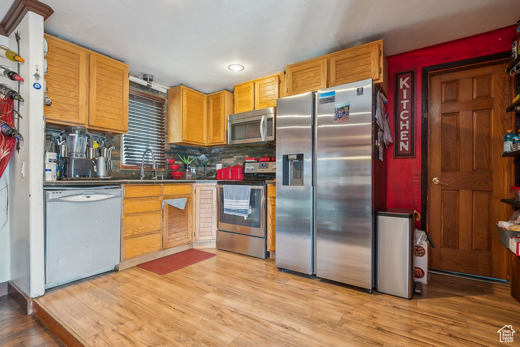 Kitchen featuring appliances with stainless steel finishes, light wood-style flooring, backsplash, and a sink