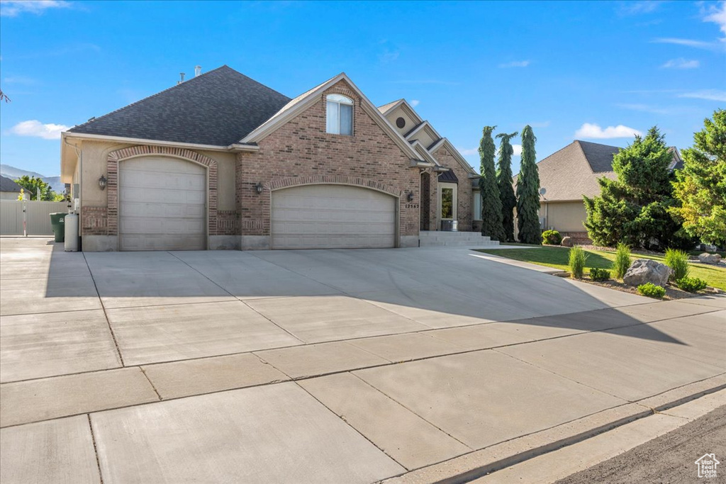 View of front facade with brick siding, driveway, an attached garage, and a shingled roof