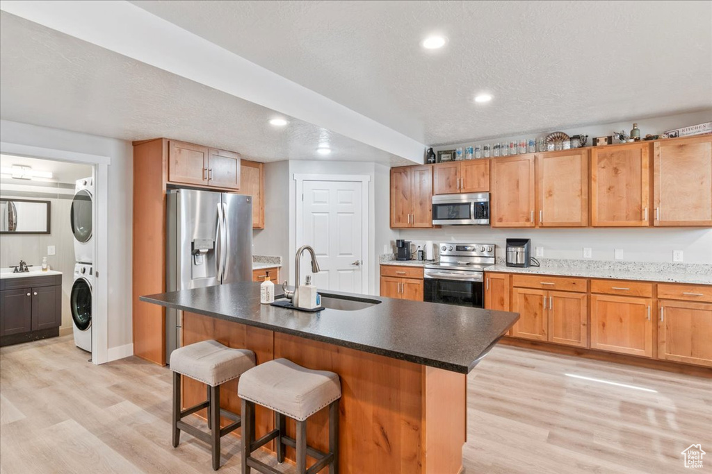 Kitchen with appliances with stainless steel finishes, stacked washer / dryer, a sink, light wood-style flooring, and recessed lighting