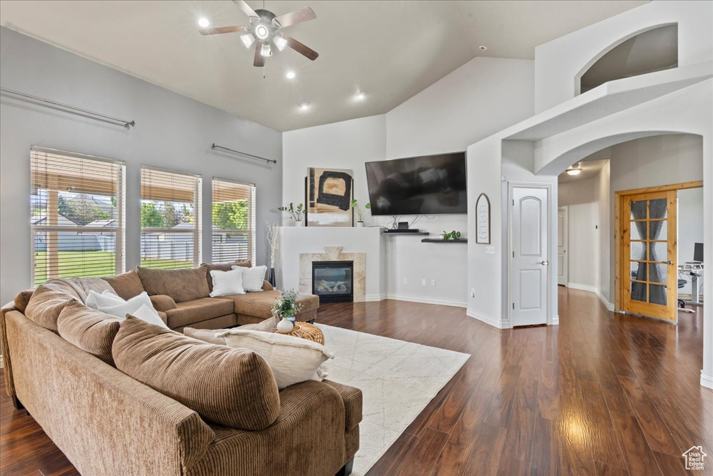 Living area featuring a ceiling fan, arched walkways, high vaulted ceiling, a high end fireplace, and dark wood finished floors