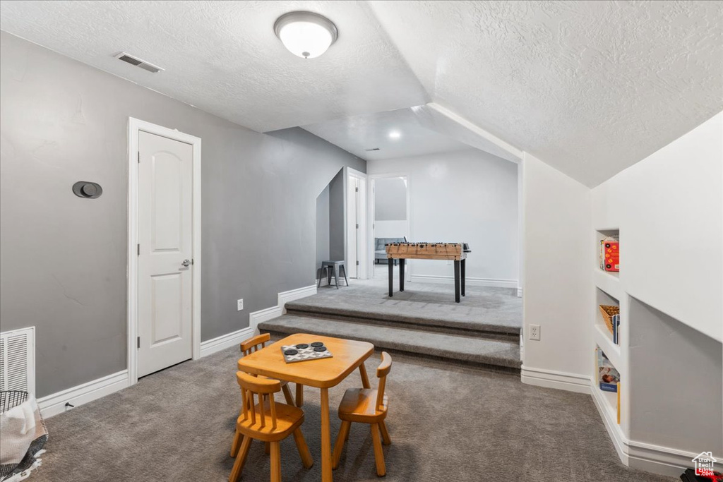 Rec room featuring a textured ceiling, carpet, vaulted ceiling, and baseboards