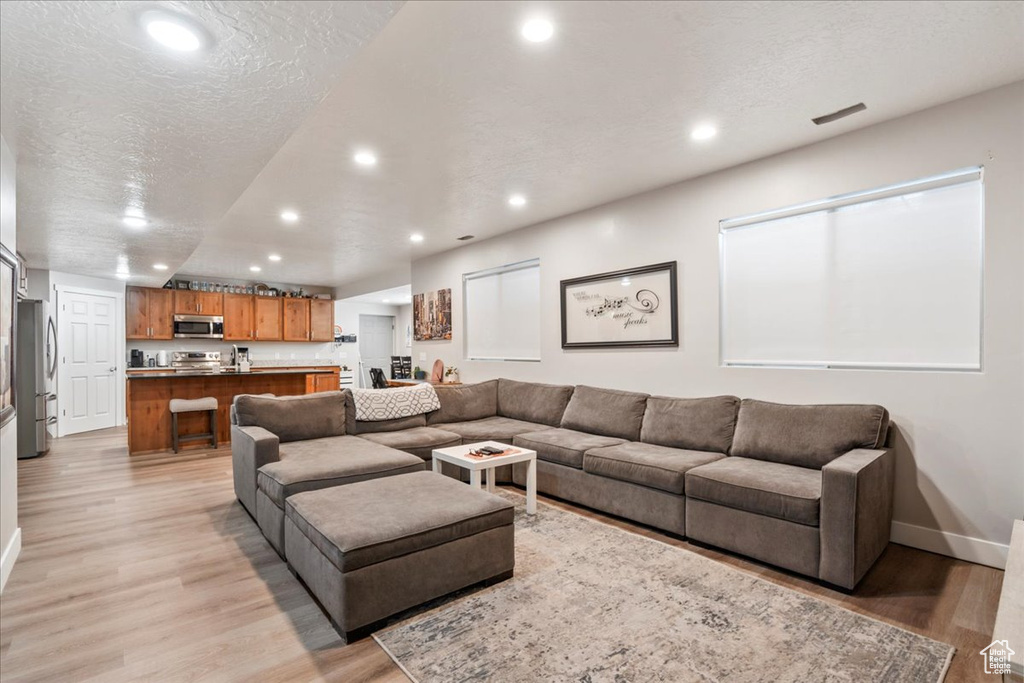 Living area featuring recessed lighting, light wood-style floors, baseboards, and a textured ceiling