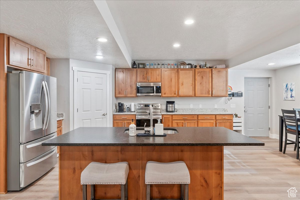Kitchen featuring stainless steel appliances, a sink, recessed lighting, light wood-style floors, and a breakfast bar area