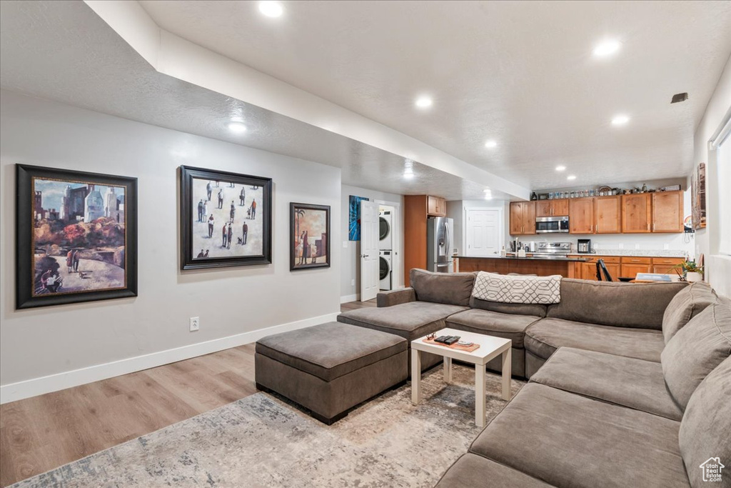 Living room featuring stacked washer / dryer, light wood-type flooring, baseboards, and recessed lighting