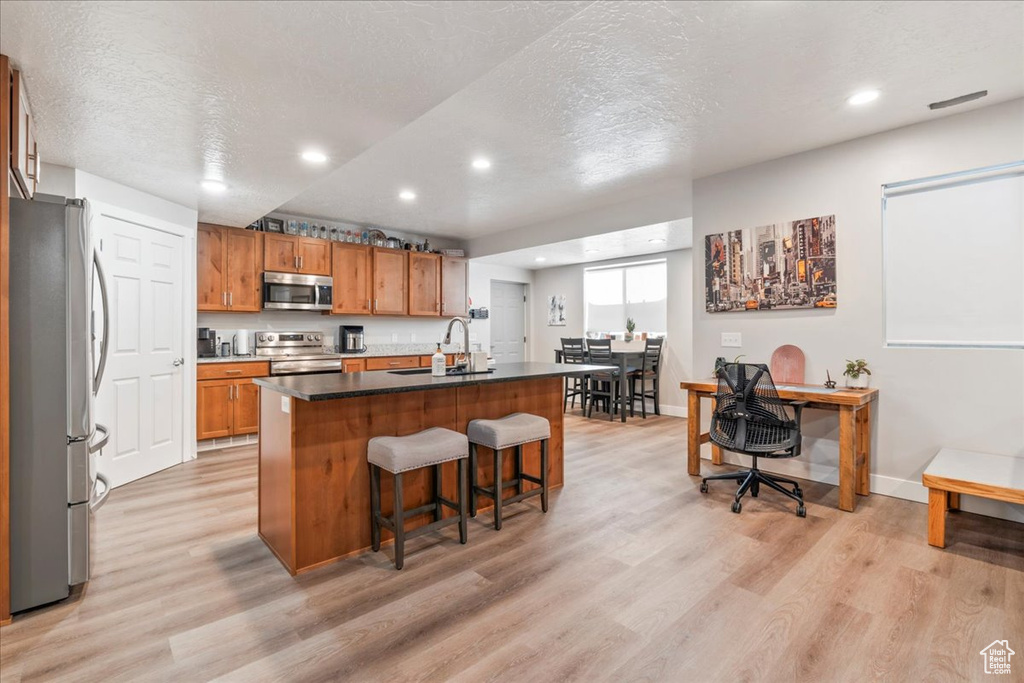 Kitchen featuring appliances with stainless steel finishes, a sink, light wood-type flooring, recessed lighting, and a breakfast bar