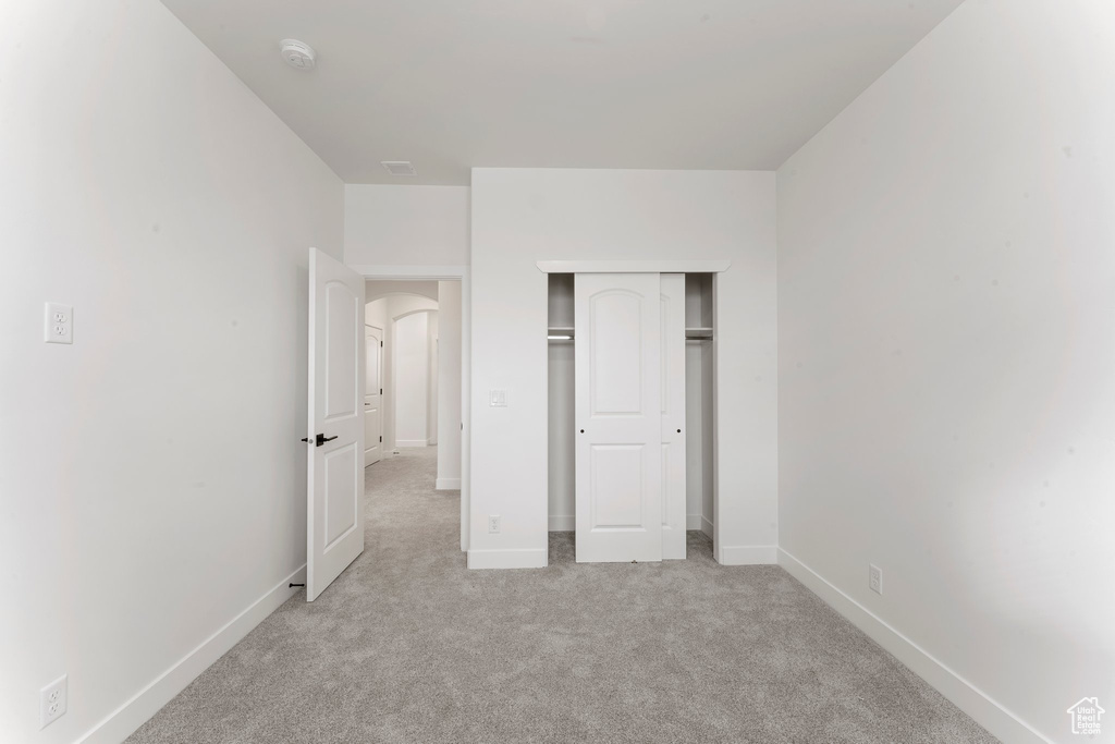 Unfurnished bedroom featuring light colored carpet, baseboards, a closet, and arched walkways