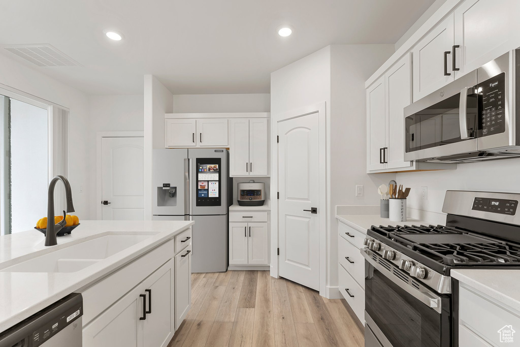 Kitchen featuring appliances with stainless steel finishes, a sink, white cabinetry, light wood finished floors, and recessed lighting