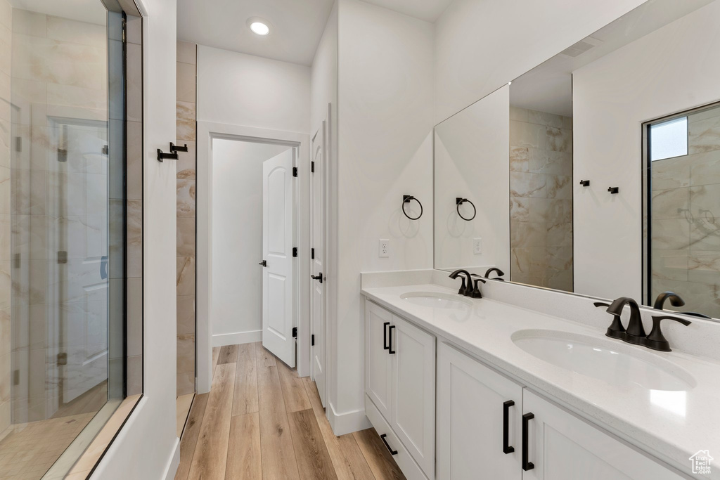 Full bathroom with double vanity, wood finished floors, tiled shower, recessed lighting, and baseboards