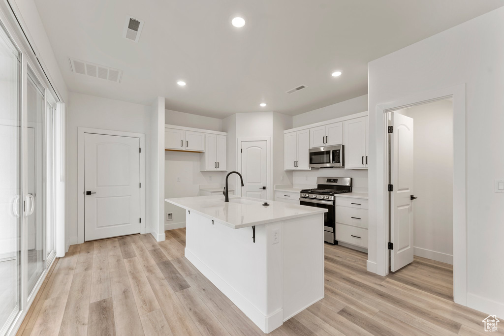 Kitchen featuring appliances with stainless steel finishes, white cabinets, light wood-style floors, baseboards, and recessed lighting