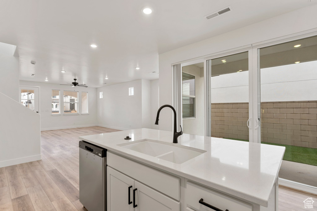 Kitchen featuring stainless steel dishwasher, a sink, open floor plan, white cabinetry, and a kitchen island with sink