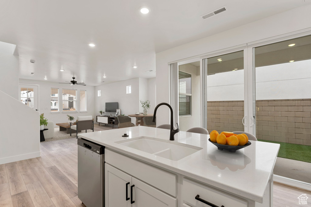 Kitchen with stainless steel dishwasher, a sink, open floor plan, light wood-type flooring, and white cabinets