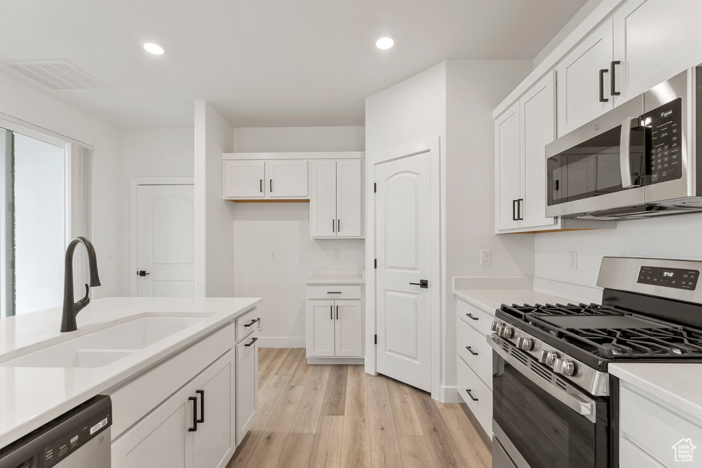 Kitchen featuring appliances with stainless steel finishes, a sink, white cabinets, light wood finished floors, and light countertops