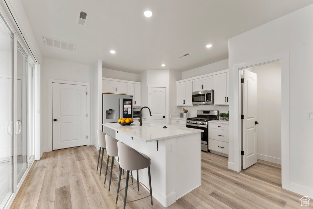 Kitchen featuring appliances with stainless steel finishes, a sink, a kitchen breakfast bar, light wood-style floors, and white cabinets