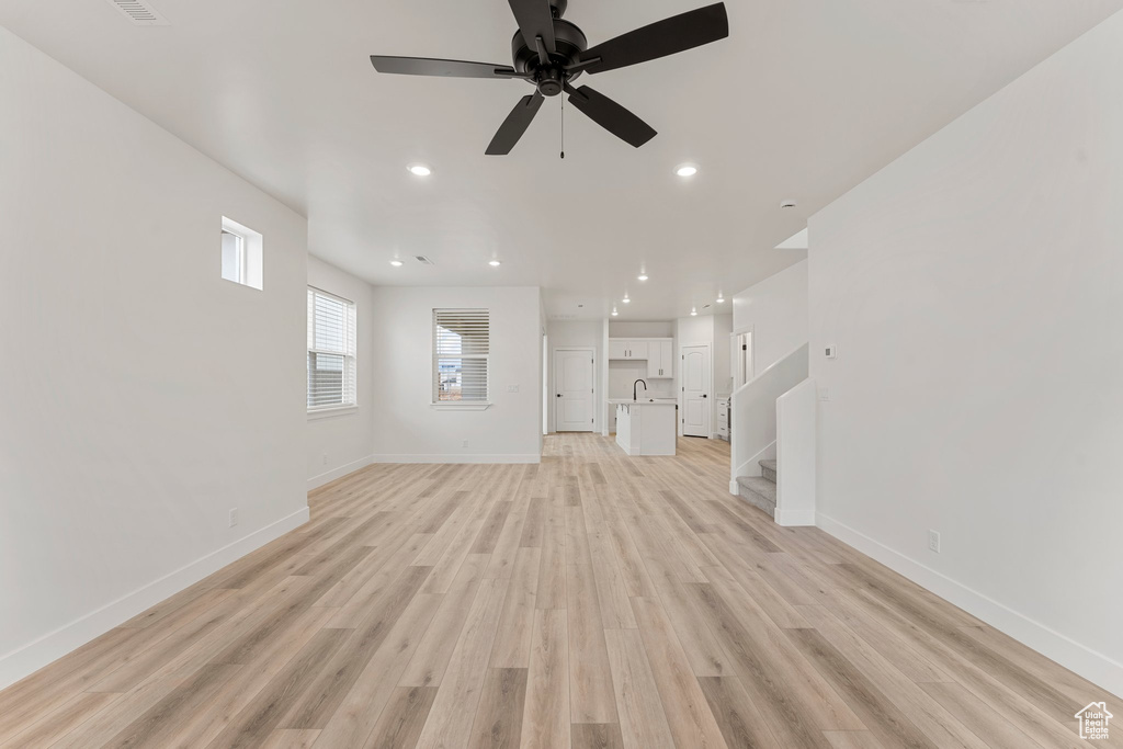 Unfurnished living room with a ceiling fan, baseboards, light wood-style flooring, stairs, and recessed lighting