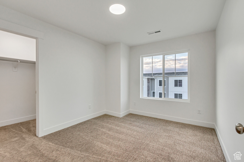 Unfurnished bedroom featuring light colored carpet, baseboards, and a walk in closet