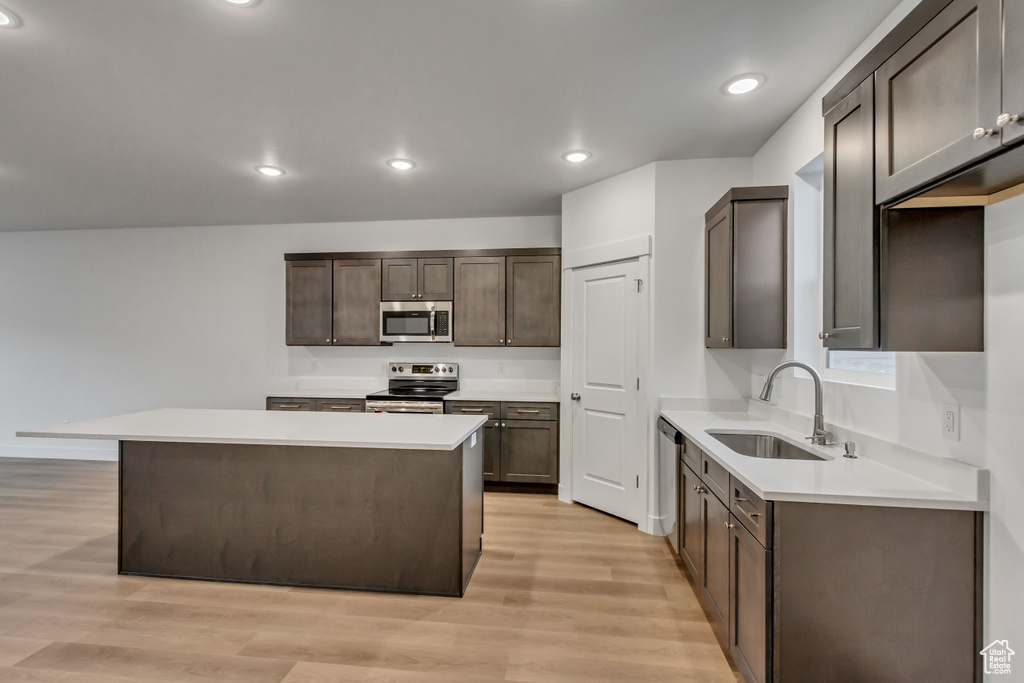 Kitchen with stainless steel appliances, a sink, light wood finished floors, a center island, and recessed lighting