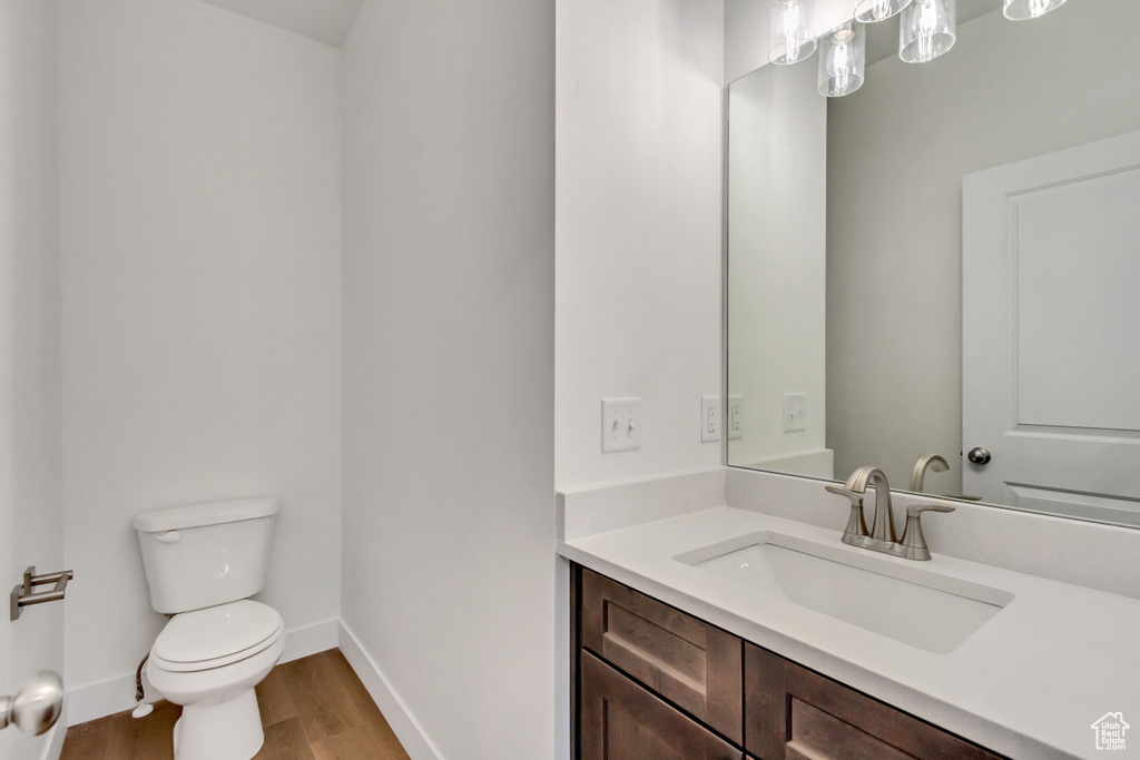 Half bathroom with wood finished floors, toilet, vanity, and baseboards