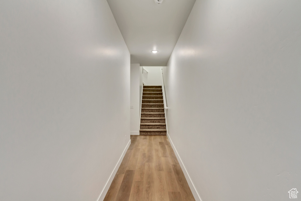 Corridor with light wood finished floors, stairs, and baseboards
