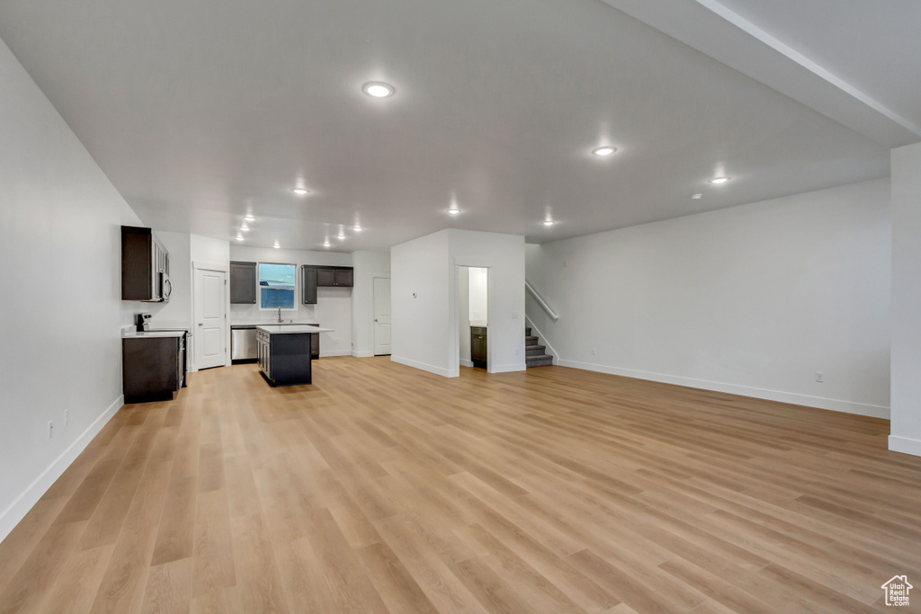 Unfurnished living room with stairway, baseboards, light wood finished floors, recessed lighting, and a sink