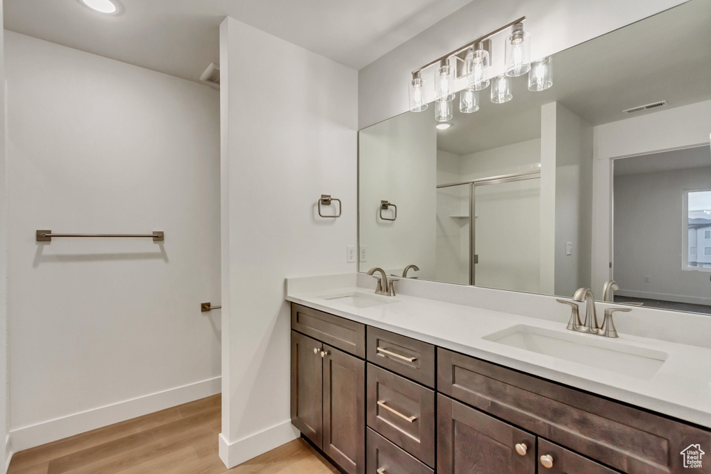 Bathroom with double vanity, baseboards, wood finished floors, and a stall shower