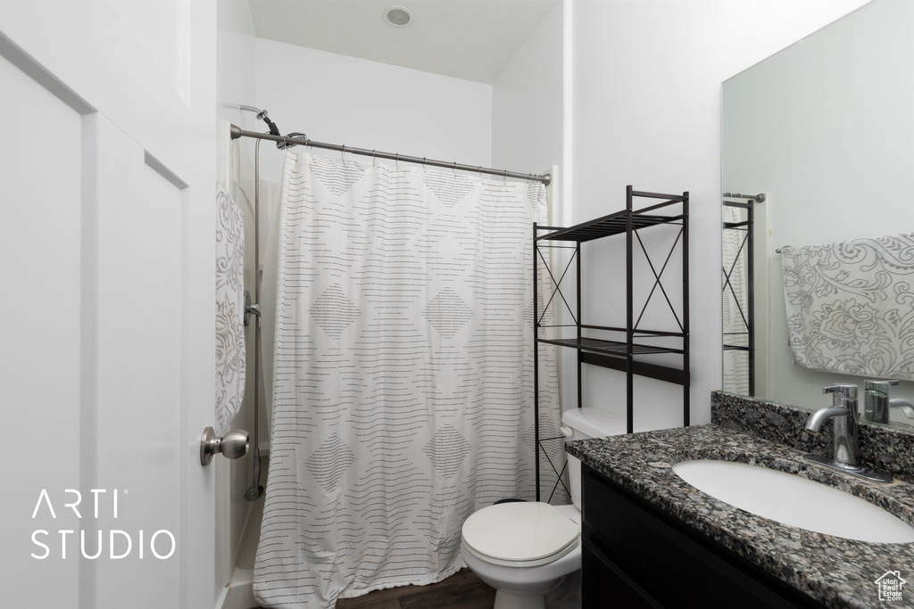Bathroom with toilet, vanity, shower / tub combo with curtain, and wood finished floors
