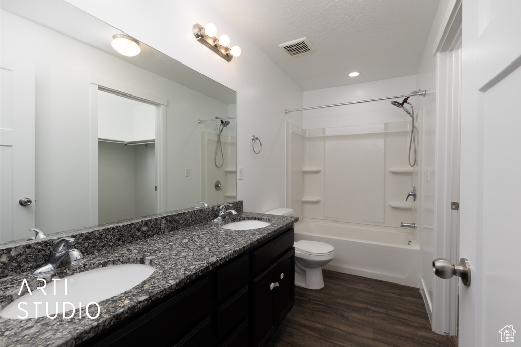 Bathroom with toilet, double vanity, shower / tub combination, wood finished floors, and a textured ceiling