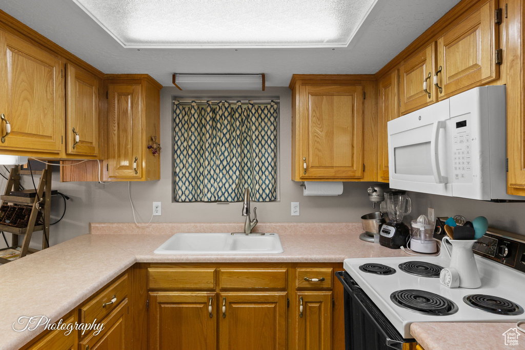 Kitchen featuring white appliances, a sink, light countertops, and brown cabinetry