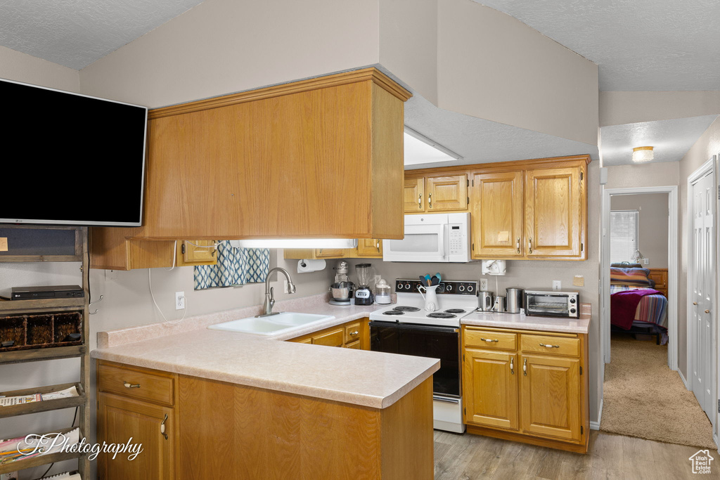 Kitchen with white appliances, a sink, light countertops, light wood-style floors, and a textured ceiling