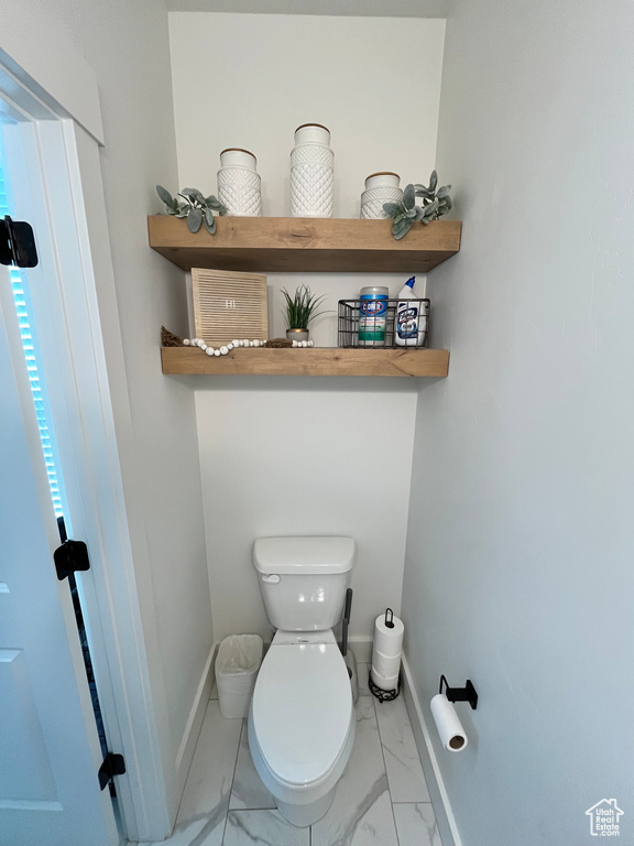 Bathroom featuring marble look tile flooring, toilet, and baseboards