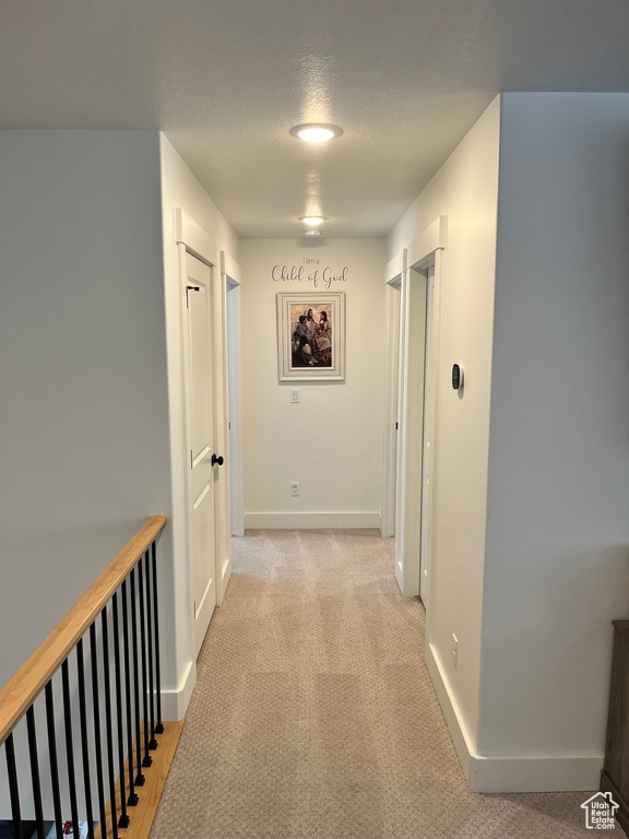 Hall featuring baseboards, a textured ceiling, and light carpet